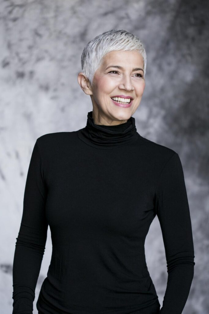 Woman with a textured salt-and-pepper pixie featuring natural silver hair and soft charcoal lowlights.